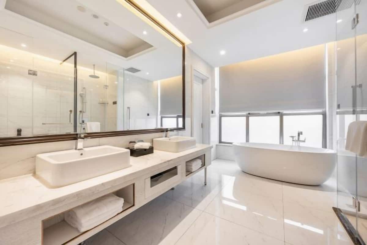 A modern bathroom with a large mirror, two sinks, a bathtub, and a glass shower enclosure.