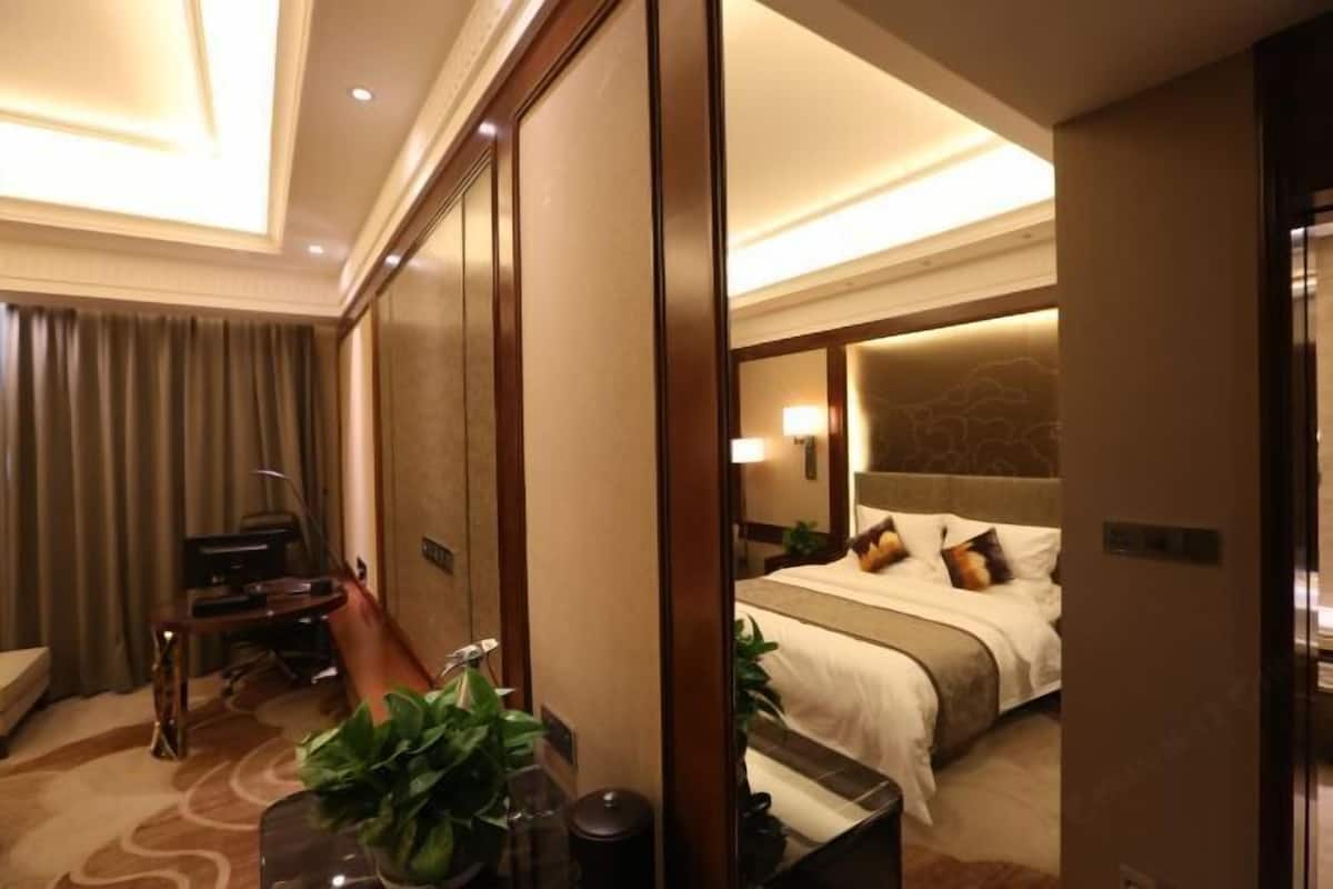A hotel room with a bed, bedside table, lamp, and a mirror reflecting the room.