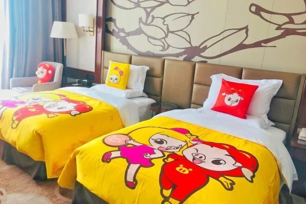 Two hotel beds with cartoon character bedspreads, a chair, and a wall with a floral pattern.