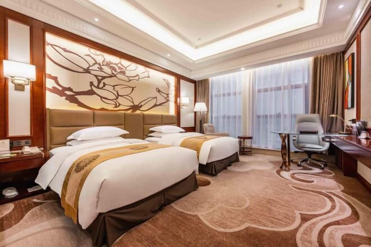 A hotel room with two beds, a desk, a chair, and a large window with curtains.