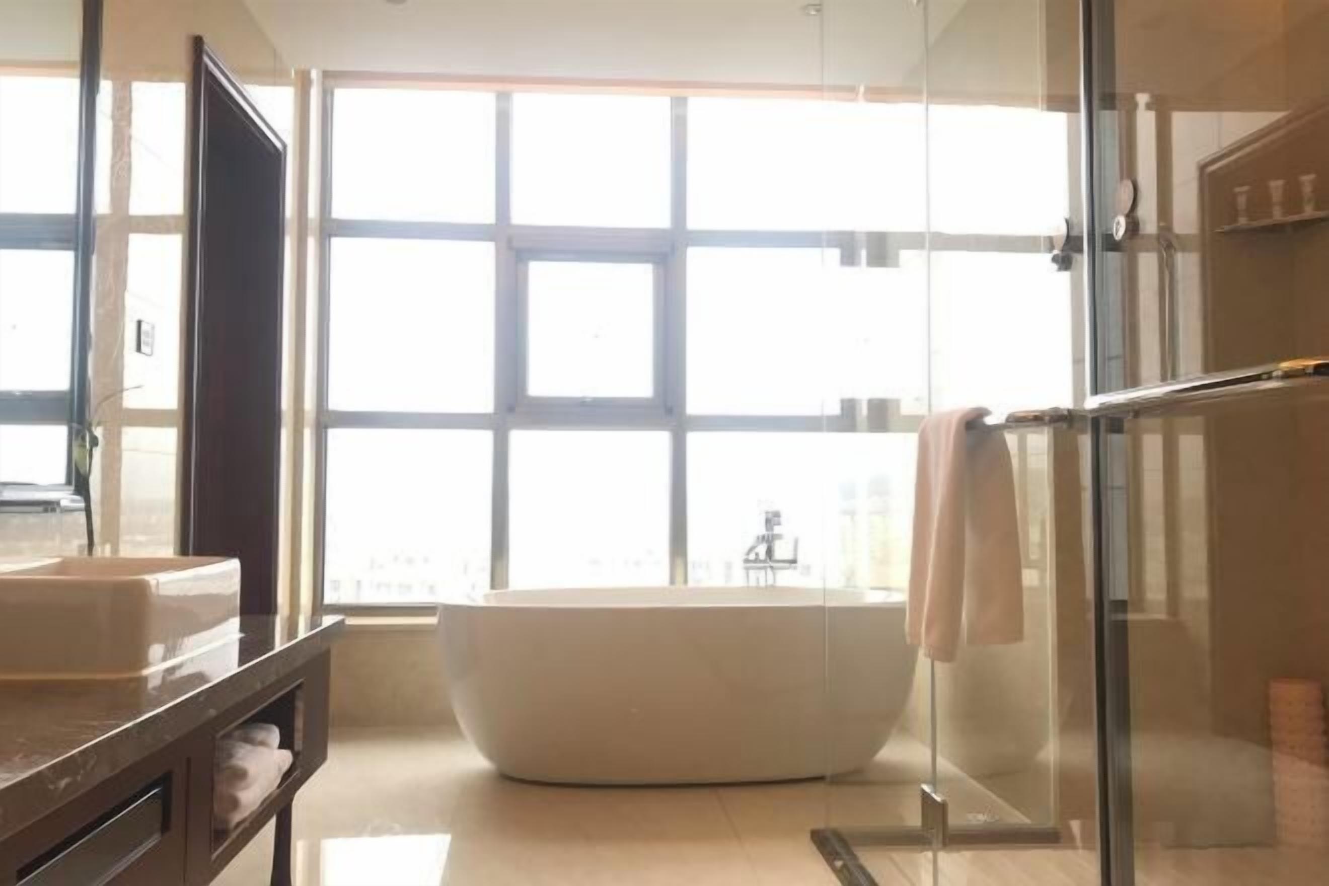 A modern bathroom with a large bathtub, a glass shower enclosure, and a large window providing natural light.