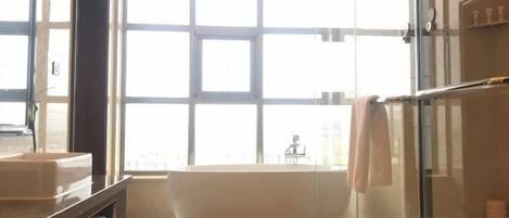 A modern bathroom with a large bathtub, a glass shower enclosure, and a large window providing natural light.