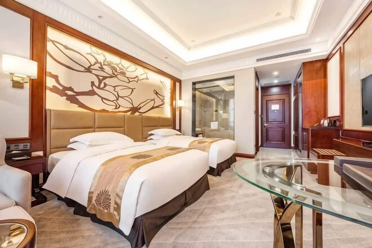 A hotel room with two beds, a glass table, a TV, and a wooden cabinet.