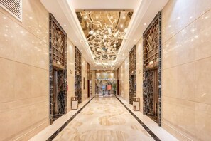 Un corredor de hotel lujoso con pisos de mármol, un diseño ornamental en el techo y decoraciones sim étricas en las paredes.