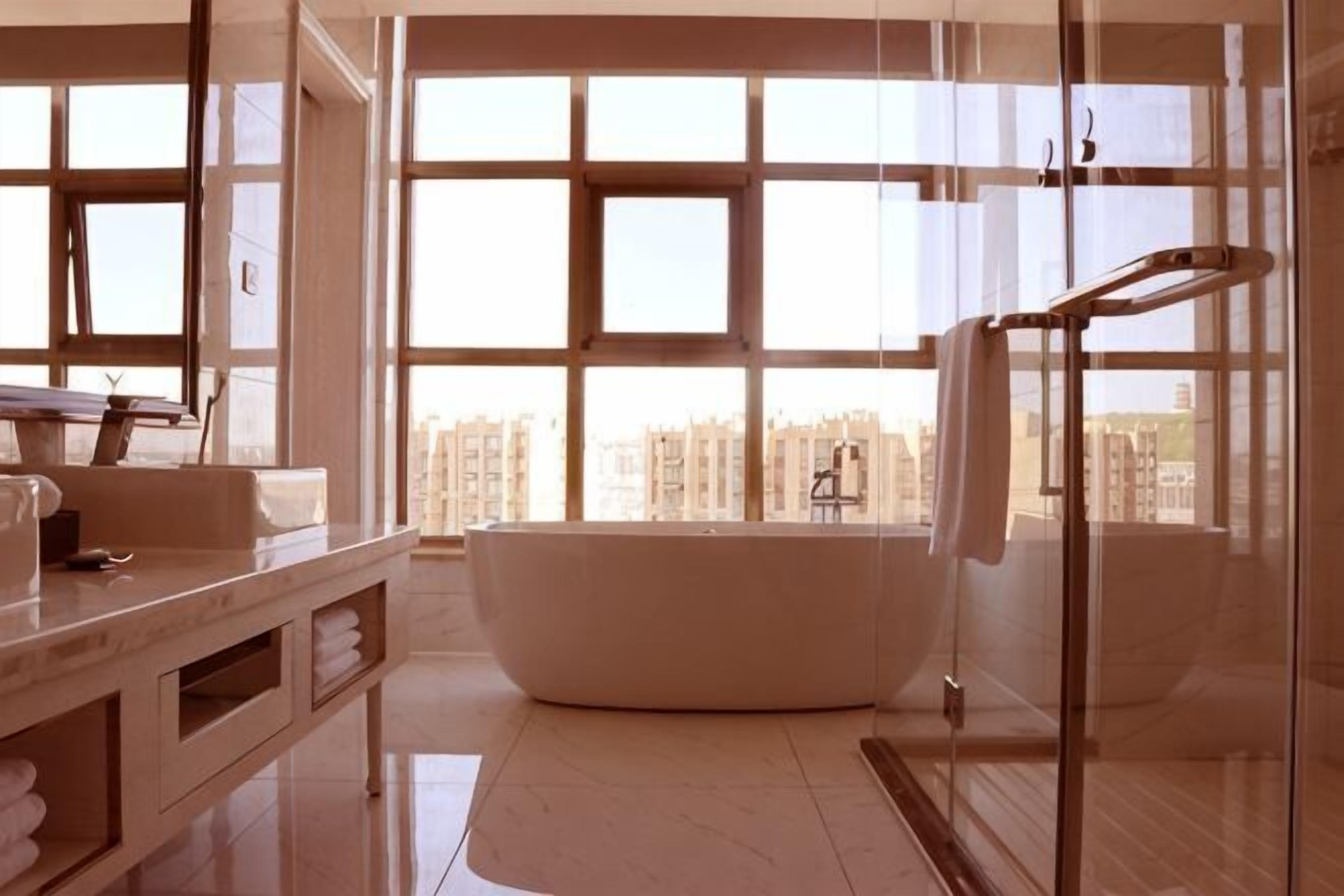 Un baño moderno con una bañera independiente, cabina de ducha de vidrio y amplias ventanas con vistas a la ciudad.