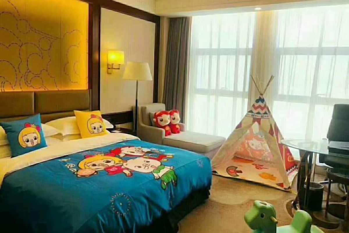 A hotel room with a bed, a desk, a chair, a lamp, a window, and a teepee.
