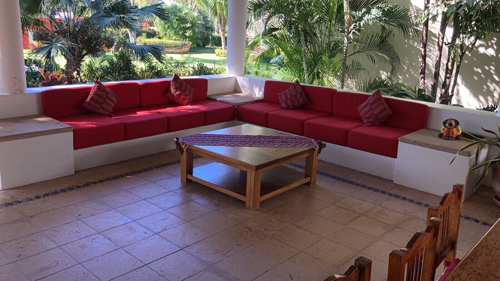 A room with a red sofa set, a wooden coffee table, and a view of a lush garden.