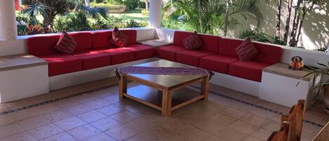 A room with a red sofa set, a wooden coffee table, and a view of a lush garden.