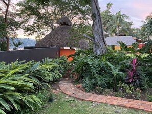 A garden pathway leading to a thatched-roof structure, surrounded by lush tropical plants and a brick border. - Casa Almendra - Perfect vacation paradise (Chacala)