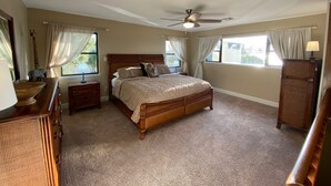 A bedroom with a large bed, a ceiling fan, a dresser, a nightstand, and a lamp. - Watch Florida sunsets from the covered lakefront dock (Minneola)