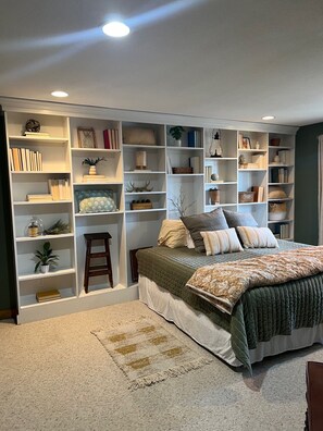 Une chambre avec un grand lit, des étagères intégrées et un petit tabouret.