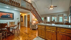 A spacious kitchen with wooden cabinets, a dining area with a round table and chairs, and a staircase leading to an upper level. - Mountain Hollow - Hot Tub (Hiawassee)