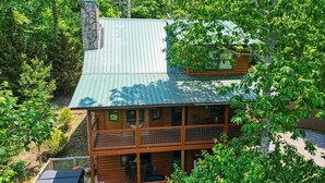 A two-story log cabin with a metal roof, surrounded by dense forest. - Mountain Hollow - Hot Tub (Hiawassee)