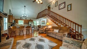A spacious living area with a large sofa, a dining table with chairs, a kitchen area, and a staircase. - Mountain Hollow - Hot Tub (Hiawassee)