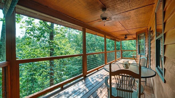 A wooden deck with a table and chairs, large windows, and a view of a forest. - Mountain Hollow - Hot Tub (Hiawassee)