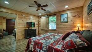 A cozy room with a bed, a television, a desk, and a window with a view of the outdoors. - Mountain Hollow - Hot Tub (Hiawassee)