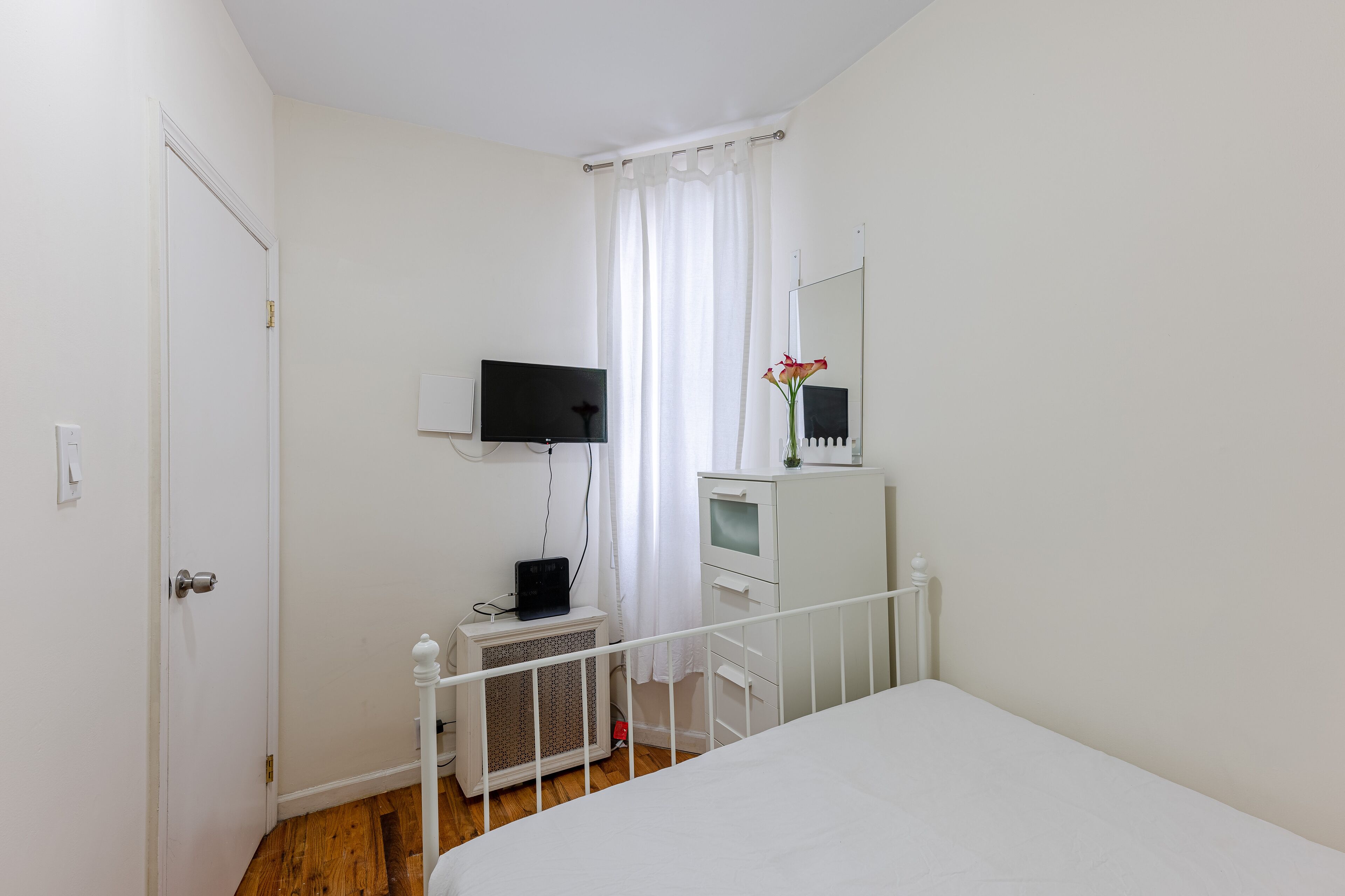 A bedroom with a bed, a TV, a small desk, and a mirror.
