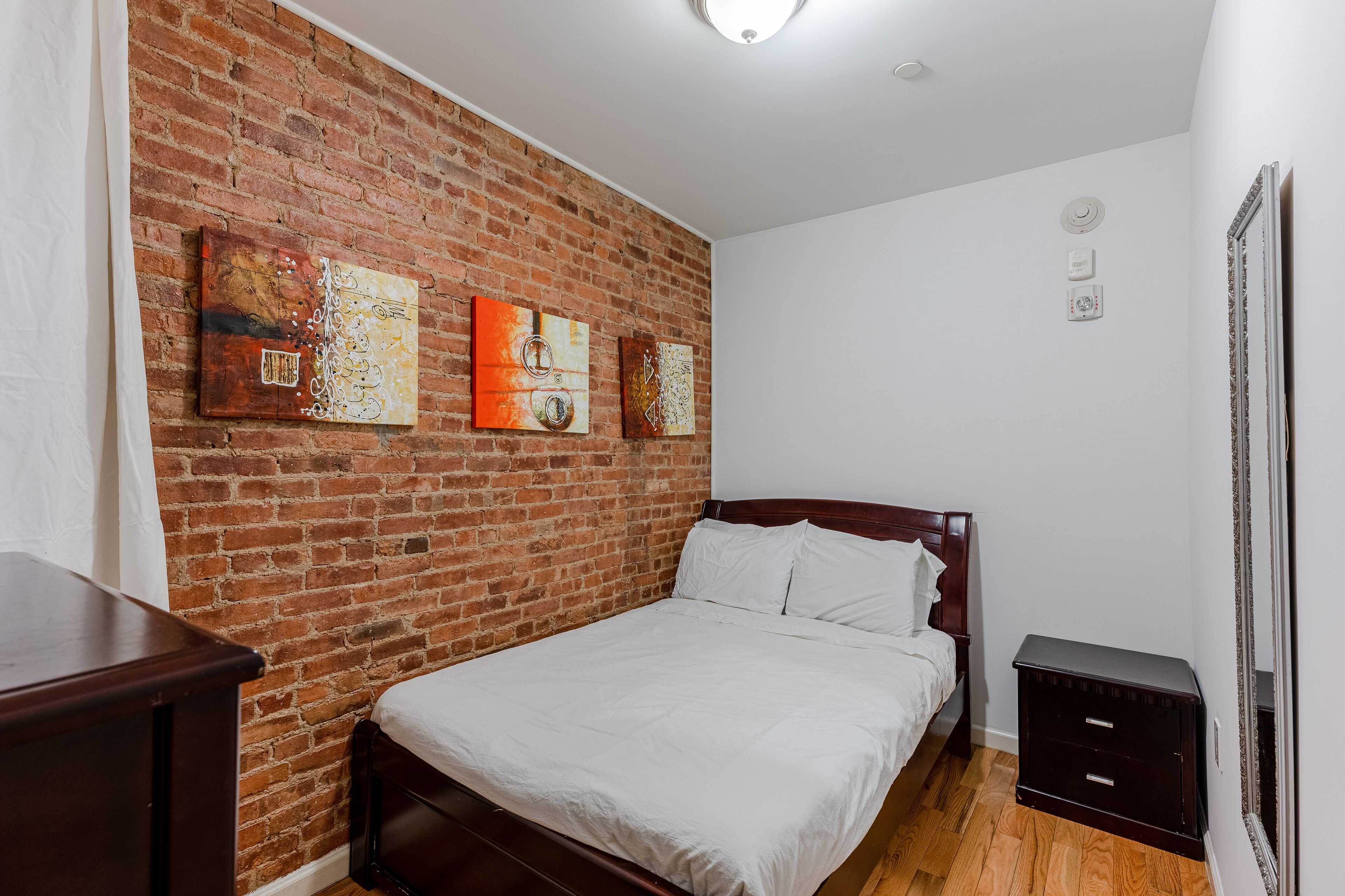 Quarto com parede de tijolos, cama de madeira, mesa de cabeceira e obras de arte.