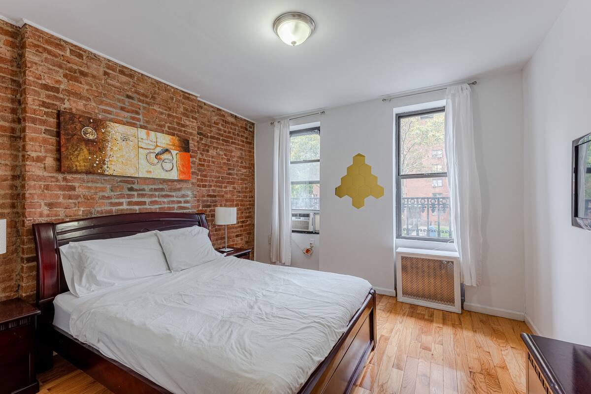 A bedroom with a brick wall, a bed, a window, and a wall art piece.