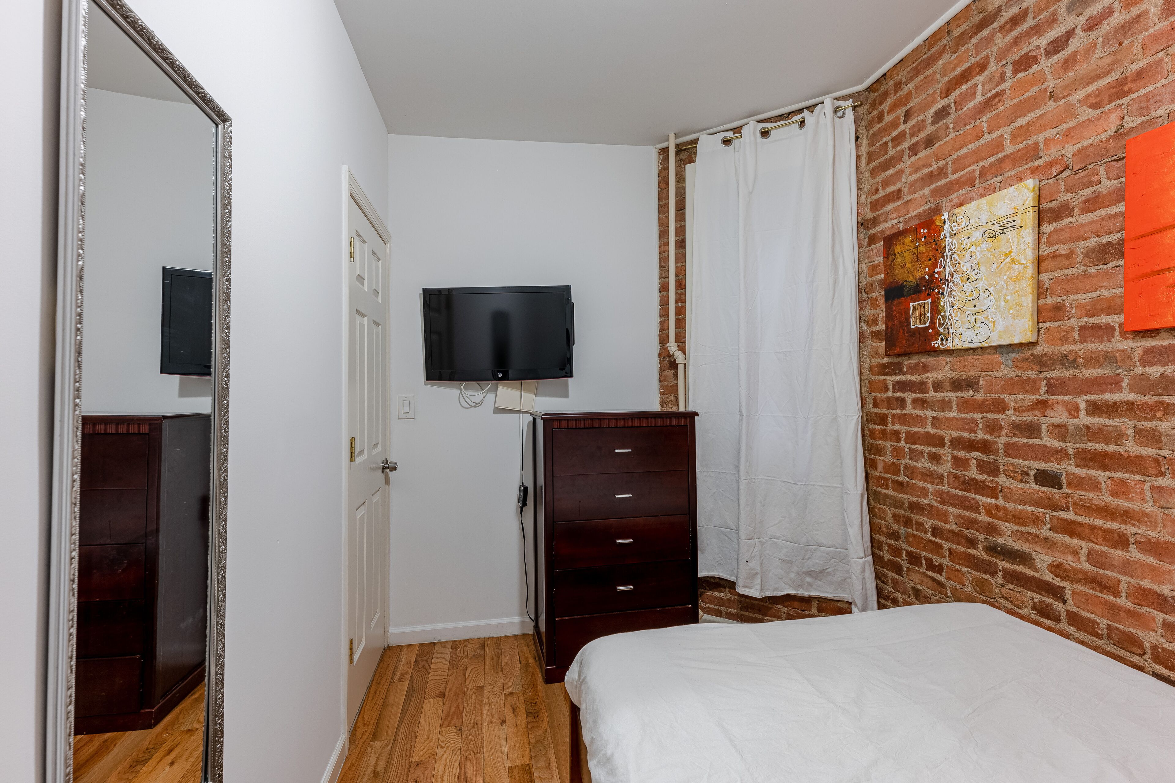 Un dormitorio con pared de ladrillo, televisor de pantalla plana, cómoda de madera, cama y espejo.