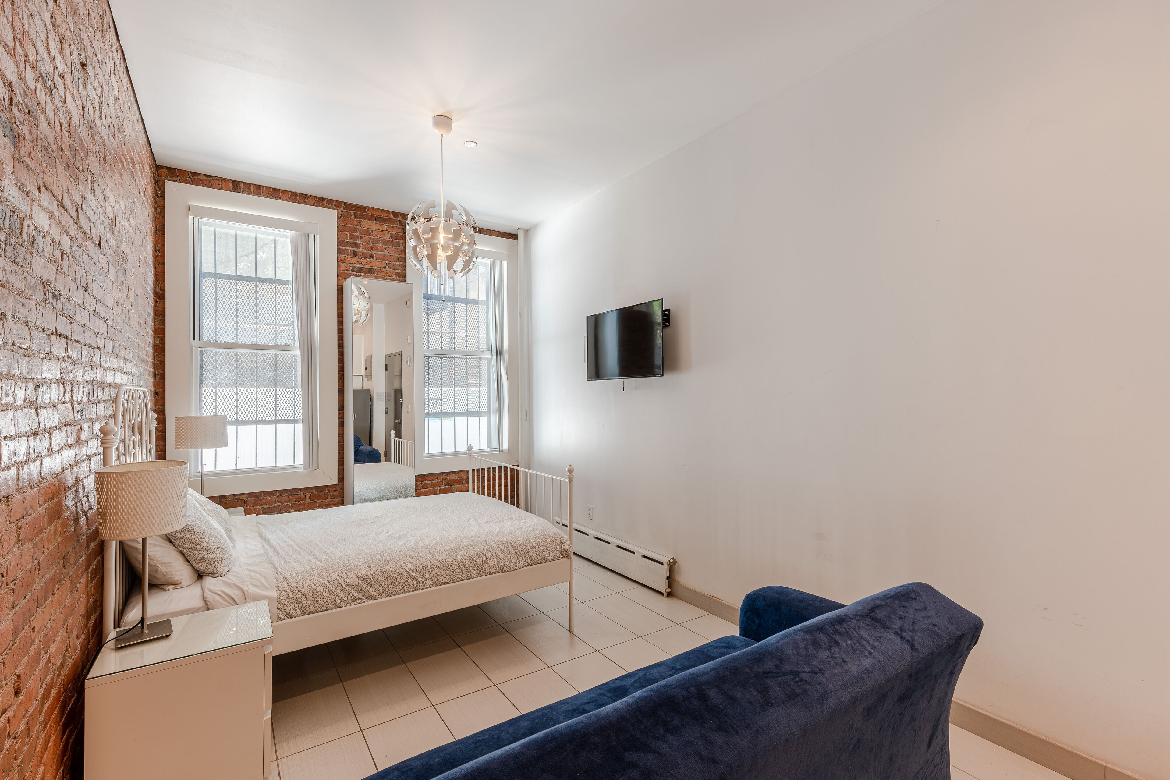 A bedroom with a bed, a TV, a mirror, and a brick wall.