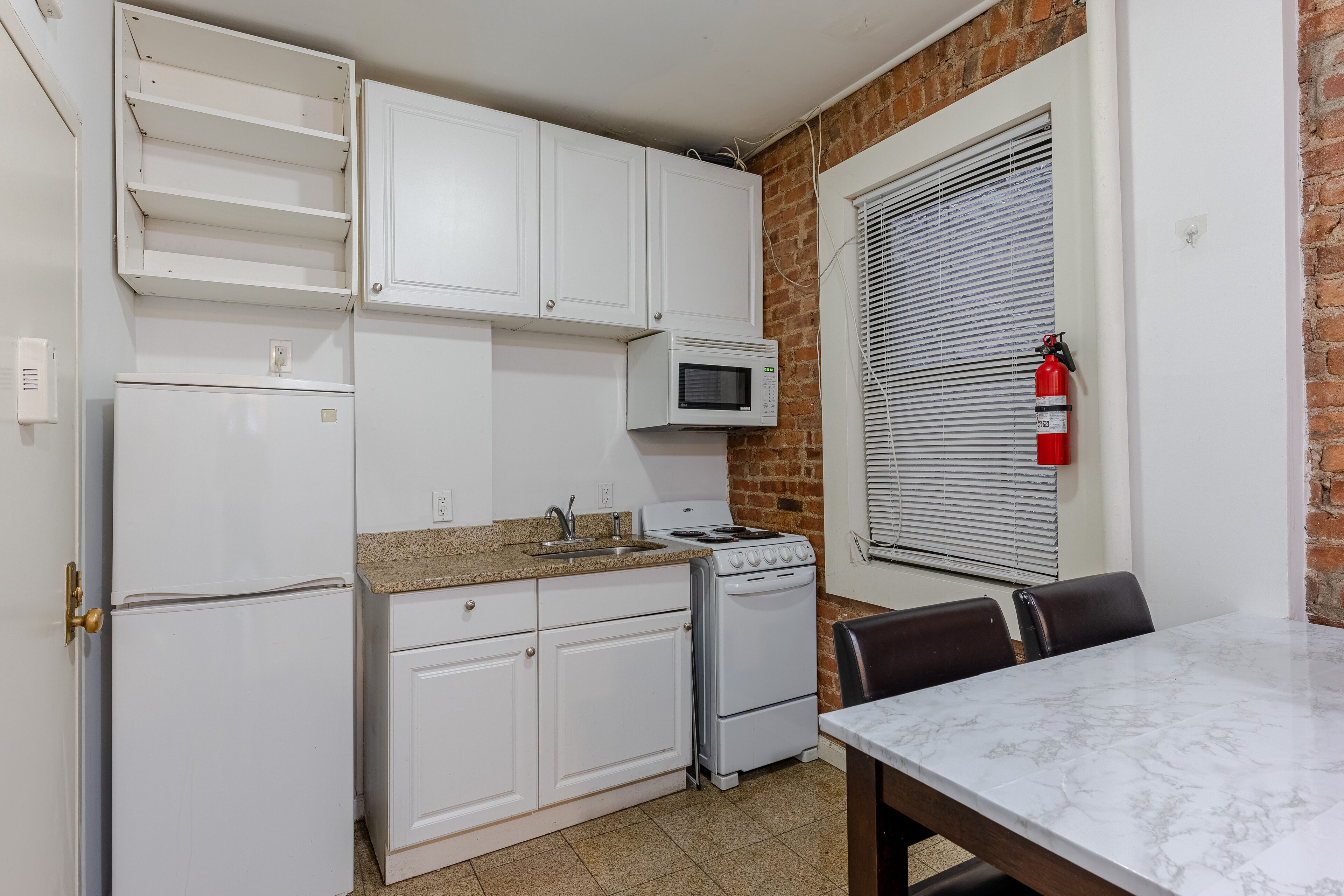 Una cocina compacta con armarios blancos, microondas, estufa y una mesa de comedor.
