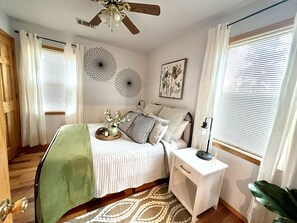 A bedroom with a bed, bedside table, nightstand, and a ceiling fan.