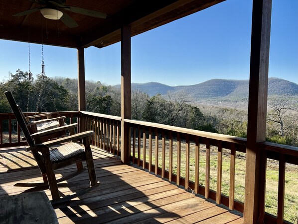 A wooden deck with a swing chair and a view of mountains.