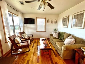 A living room with a wooden floor, a ceiling fan, a sofa, two rocking chairs, and a coffee table.