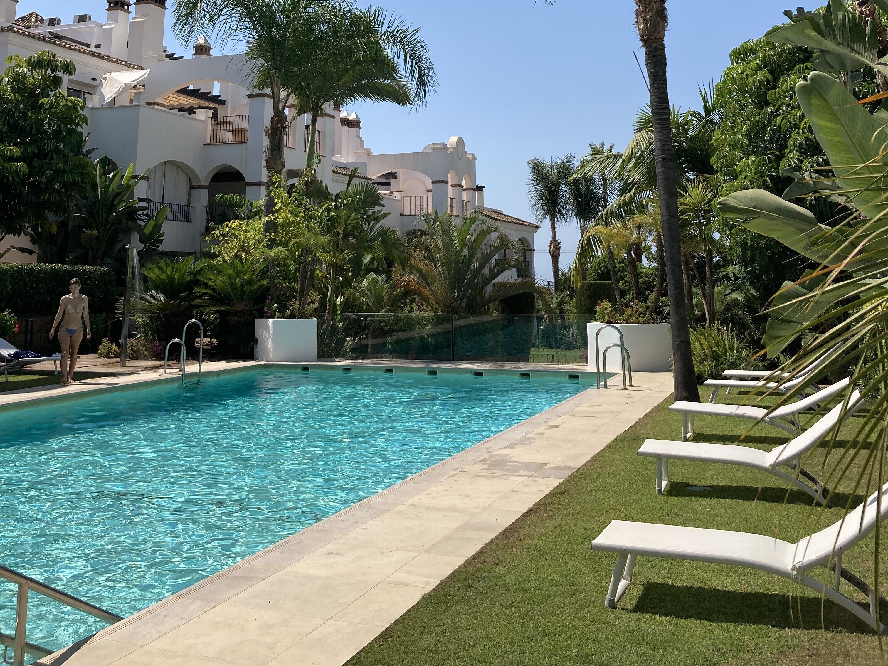 Une piscine à l’eau d’un bleu cristallin, entourée de chaises longues blanches et de palmiers.