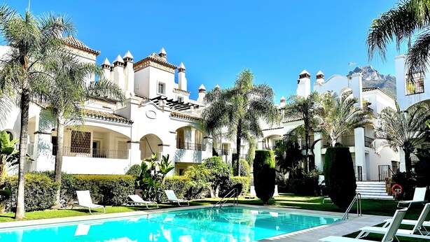 A swimming pool with lounge chairs, surrounded by palm trees and a building with multiple balconies. - Exclusive Duplex Penthouse with panoramic views  (Marbella)