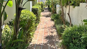 A paved pathway flanked by lush greenery and a white building with arches. - Exclusive Duplex Penthouse with panoramic views  (Marbella)