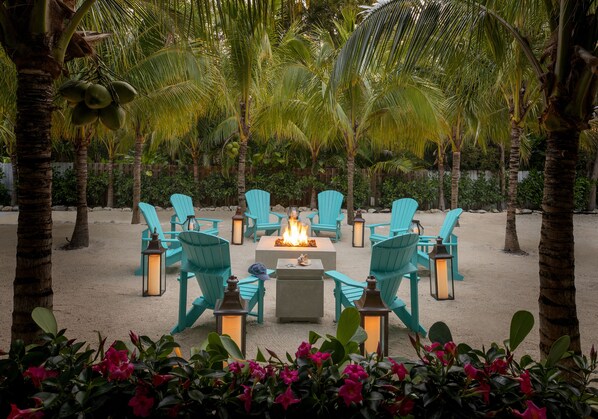 Un espace de détente aménagé sur la plage, avec des chaises turquoise, un foyer central et des lanternes.