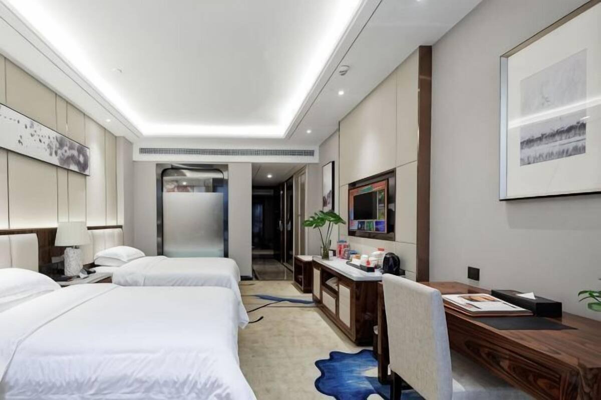 Hotelkamer met twee bedden, een bureau, een stoel, een televisie en een badkamer zichtbaar door een geopende deur.