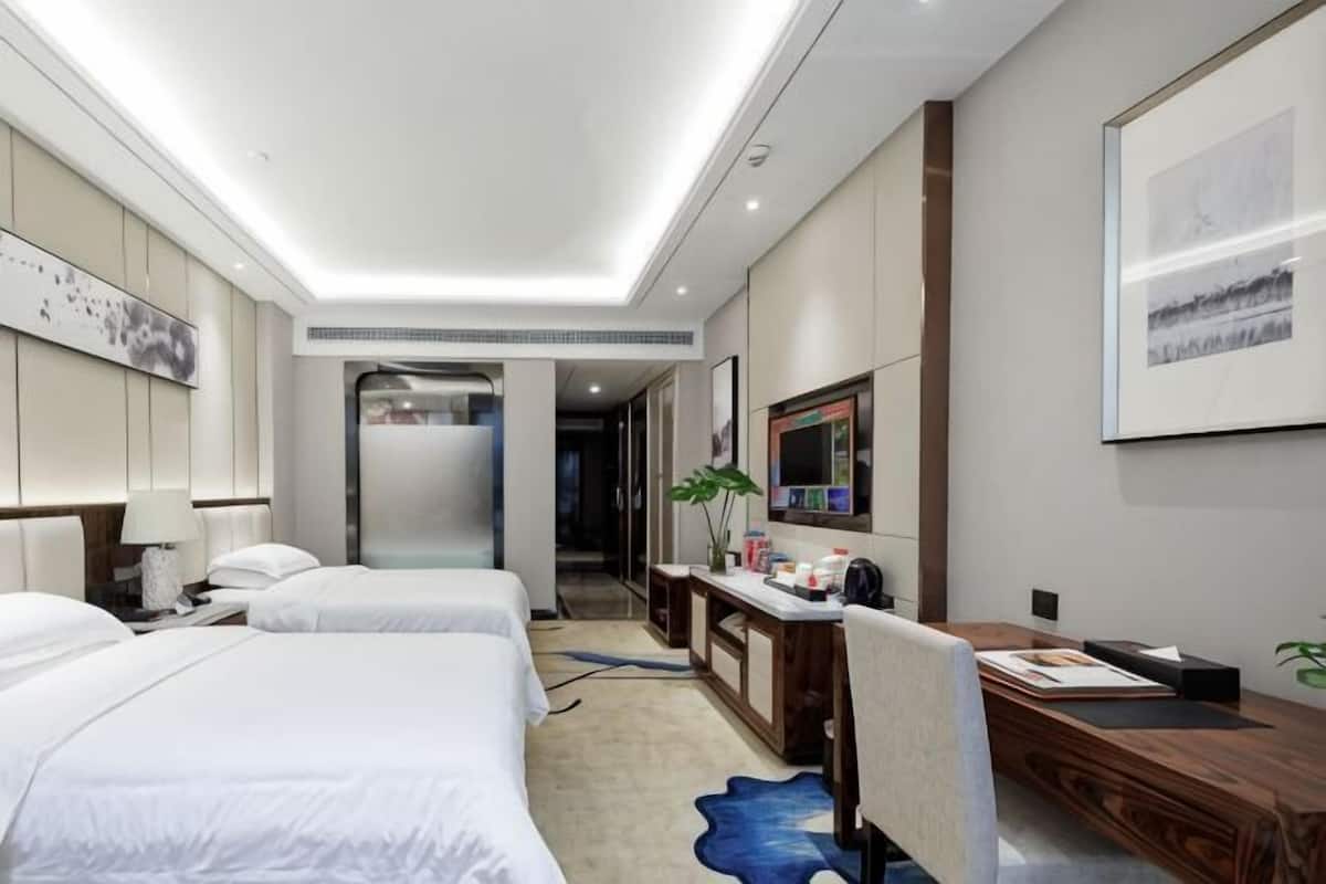 A hotel room with two beds, a desk, a chair, a TV, and a bathroom visible through an open door.
