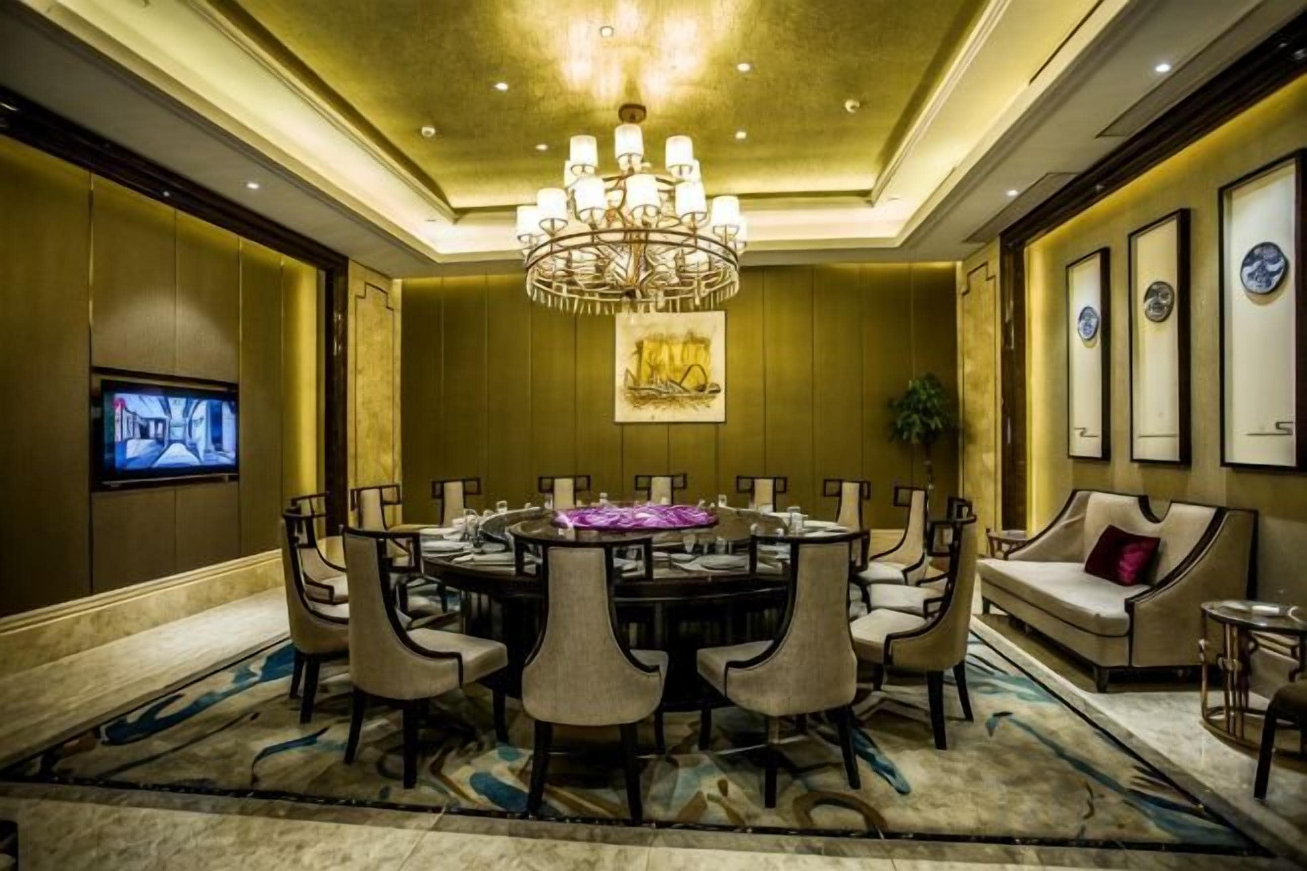 A conference room with a round table, chairs, a chandelier, and a television on the wall.