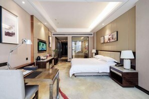 A modern hotel room with a bed, desk, and chair, a TV, and artwork on the walls.