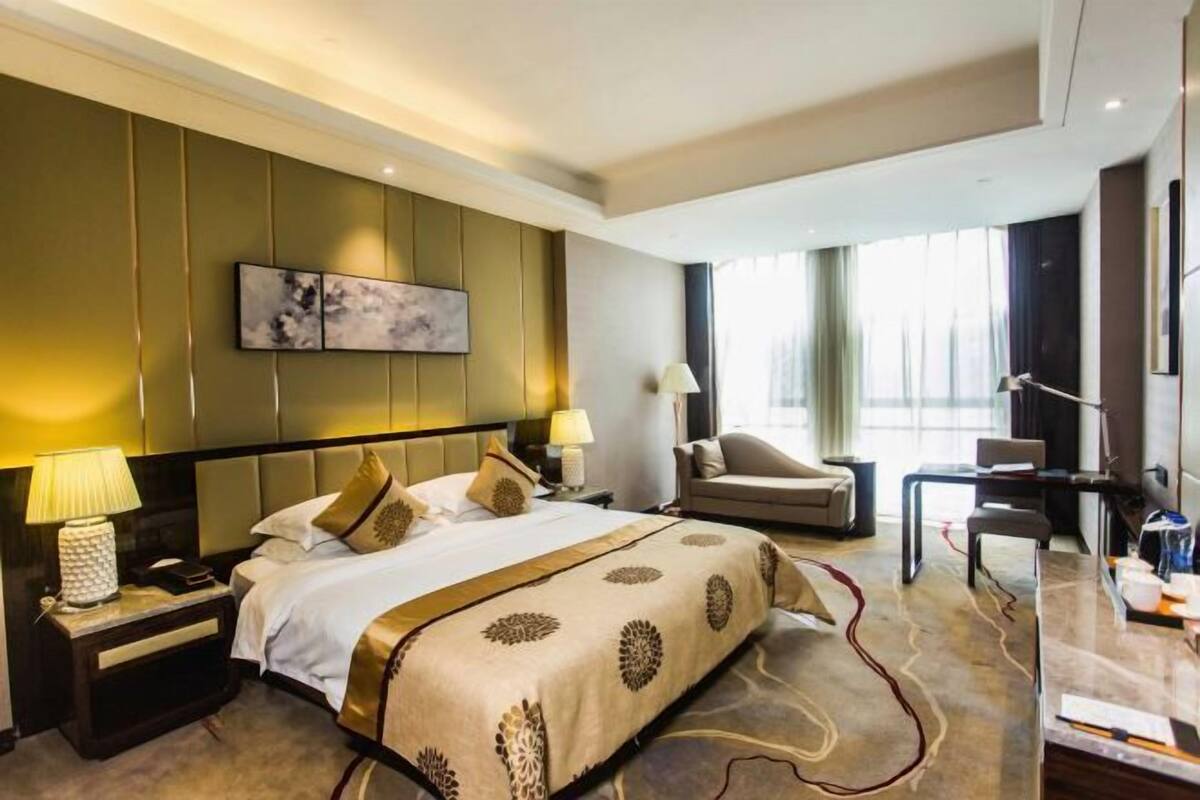 Een hotelkamer met een groot bed, een bureau, een stoel, een televisie en een schilderij aan de muur.
