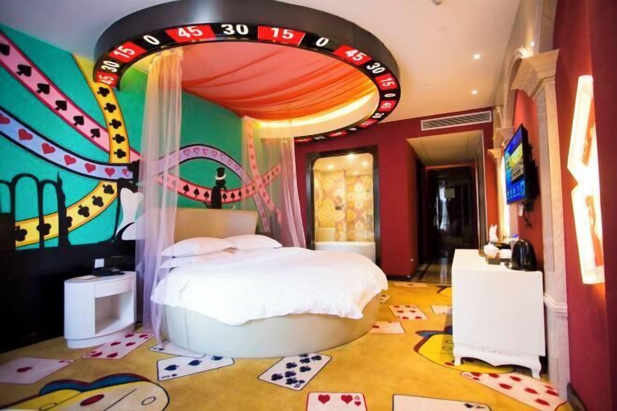 Een kamer met een bed onder een hemelbed, een roulette wiel aan de muur en speelkaarten op de vloer.