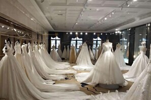 A room with multiple wedding dresses on mannequins, a carpeted floor, and large windows. - Binhu Hotel (Hanchuan)