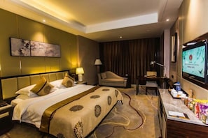 A hotel room with a large bed, a desk, a chair, a TV, and a minibar. - Binhu Hotel (Hanchuan)