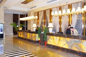 A hotel reception area with a marble counter, multiple light fixtures, and potted plants. - Binhu Hotel (Hanchuan)