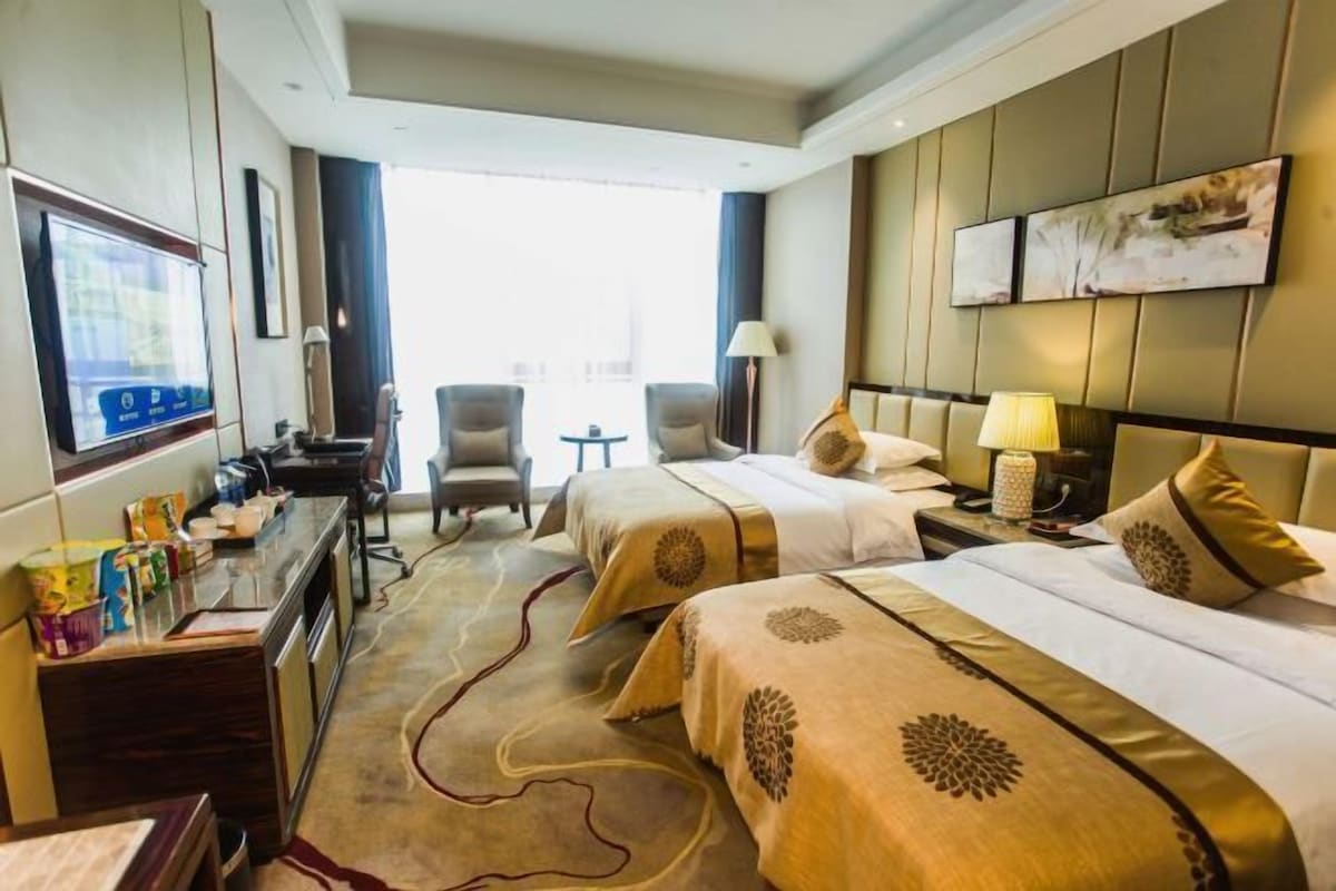 A hotel room with two beds, a desk with a computer, a chair, and a small table.