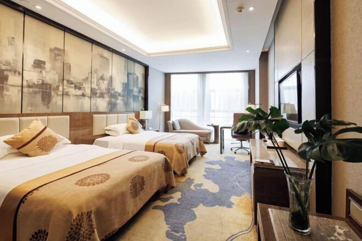 Een hotelkamer met twee bedden, een bureau, een stoel en een groot raam.