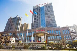 A modern building with a prominent entrance, multiple flags, and a statue in front. - Binhu Hotel (Hanchuan)