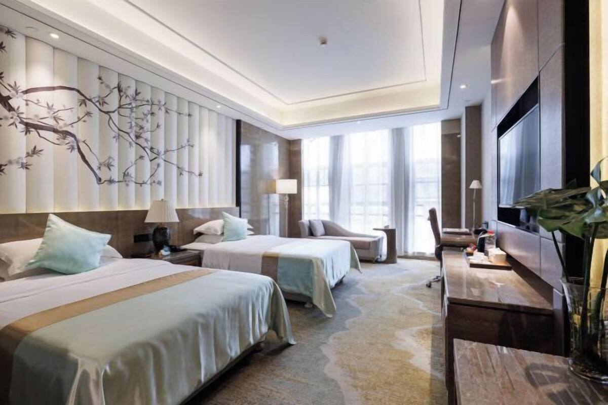 Een hotelkamer met twee bedden, een bureau, een televisie en een groot raam.