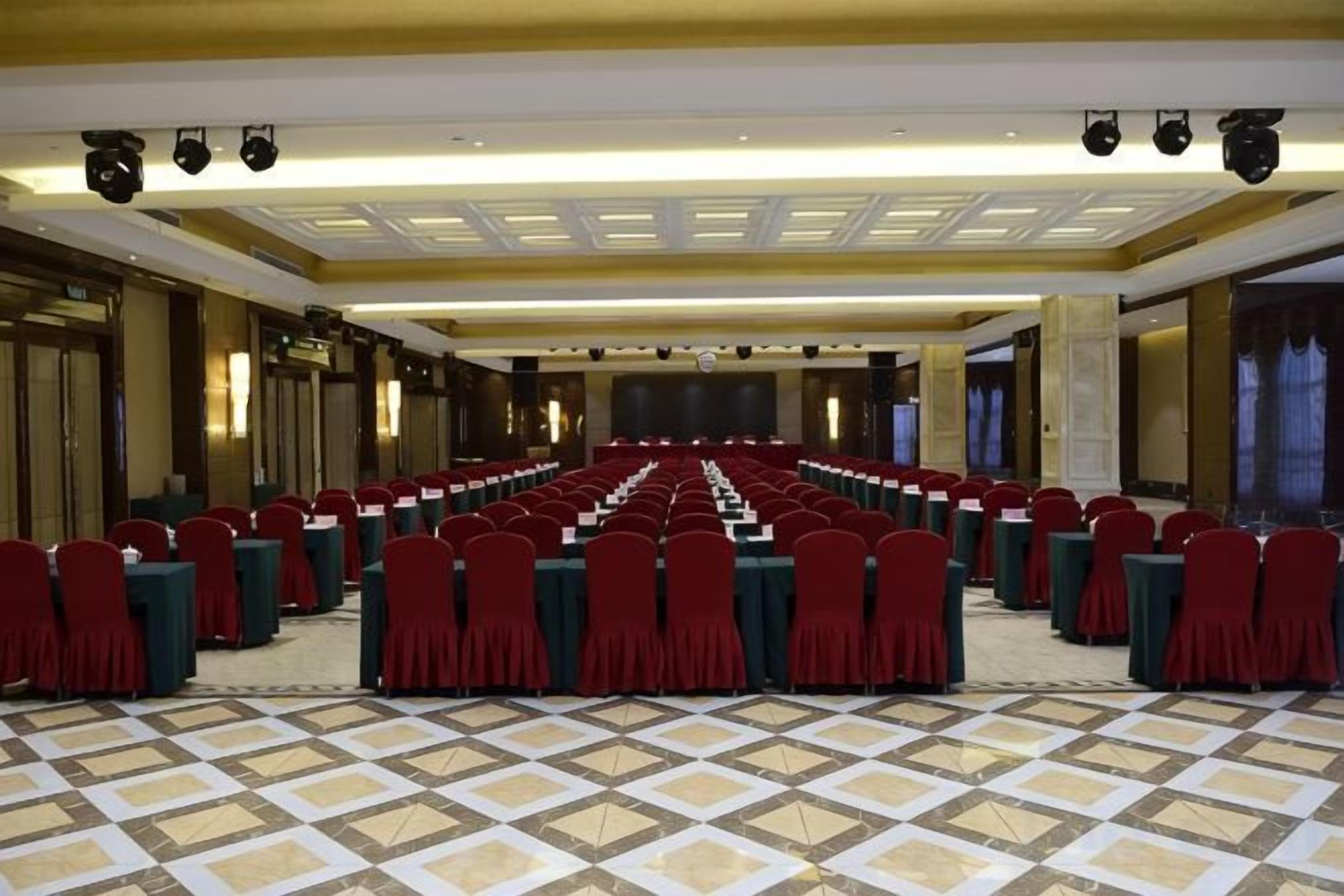 A large conference room with rows of tables and chairs, a stage, and a patterned floor.