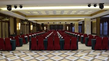 A large conference room with rows of tables and chairs, a stage, and a patterned floor.