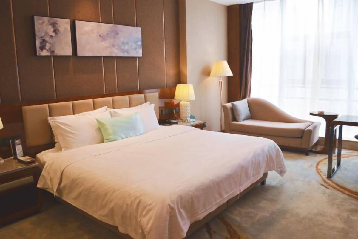 Een hotelkamer met een groot bed, een stoel, een nachtkastje en een lamp. Twee schilderijen hangen aan de muur.