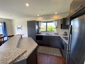 Eine moderne Küche mit Granit Arbeitsplatten, dunklen Schränken, einem Edelstahl-Kühlschrank und einem Fenster mit Vorhängen.